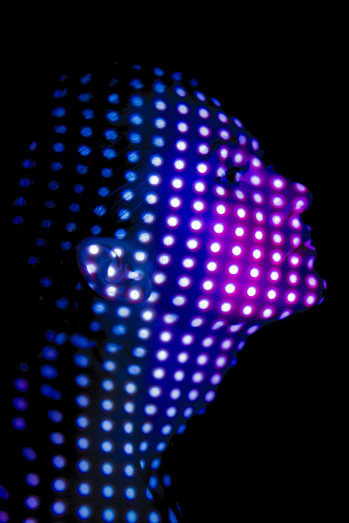 Artistic side profile portrait of a woman with vibrant purple and blue dot light projections on her face.