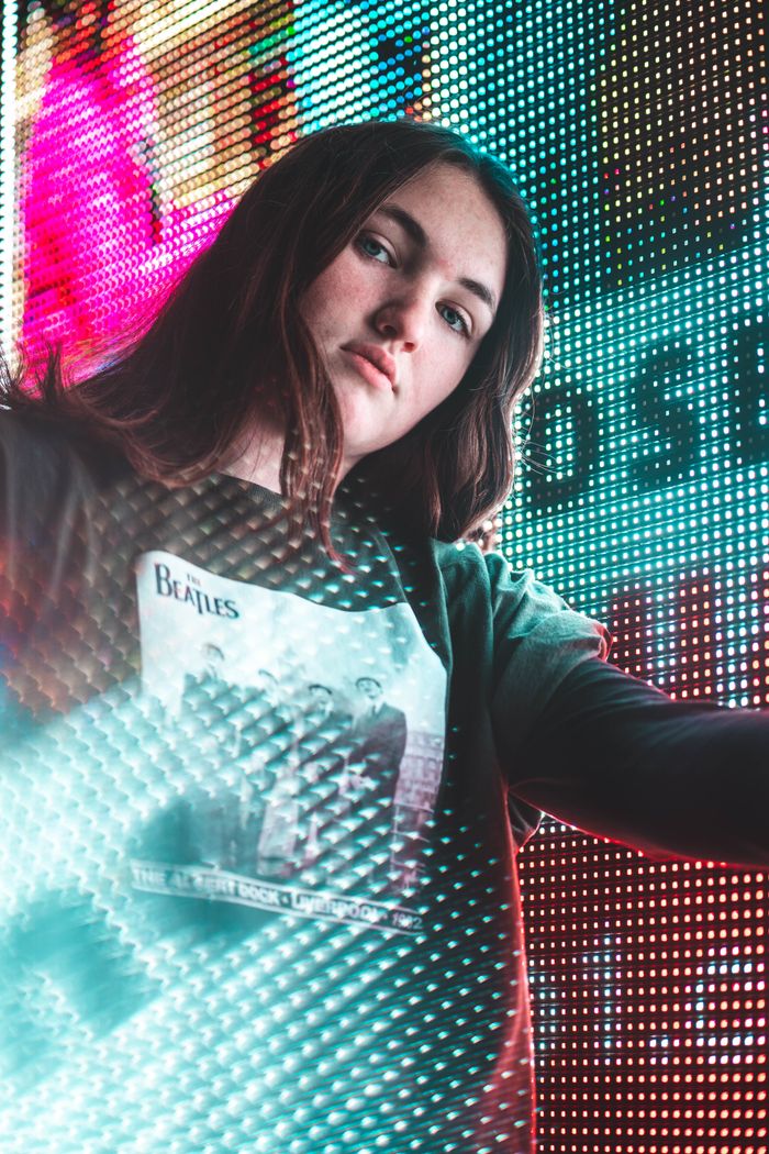 gallery-3 Portrait of a young woman wearing a band tee, posed against a vibrant digital background.